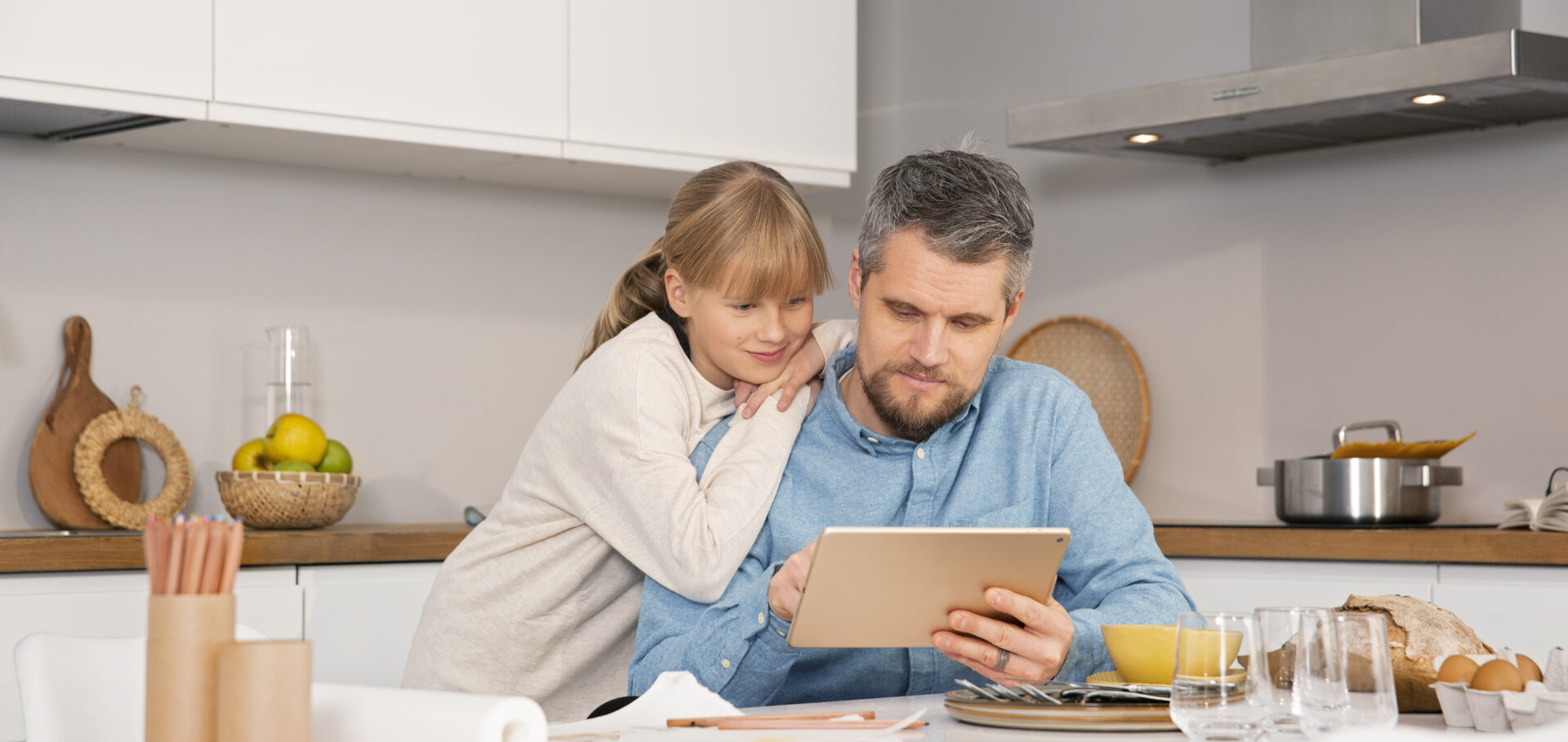 Mies selaa tablettia pöydän ääressä yhdessä lapsen kanssa.