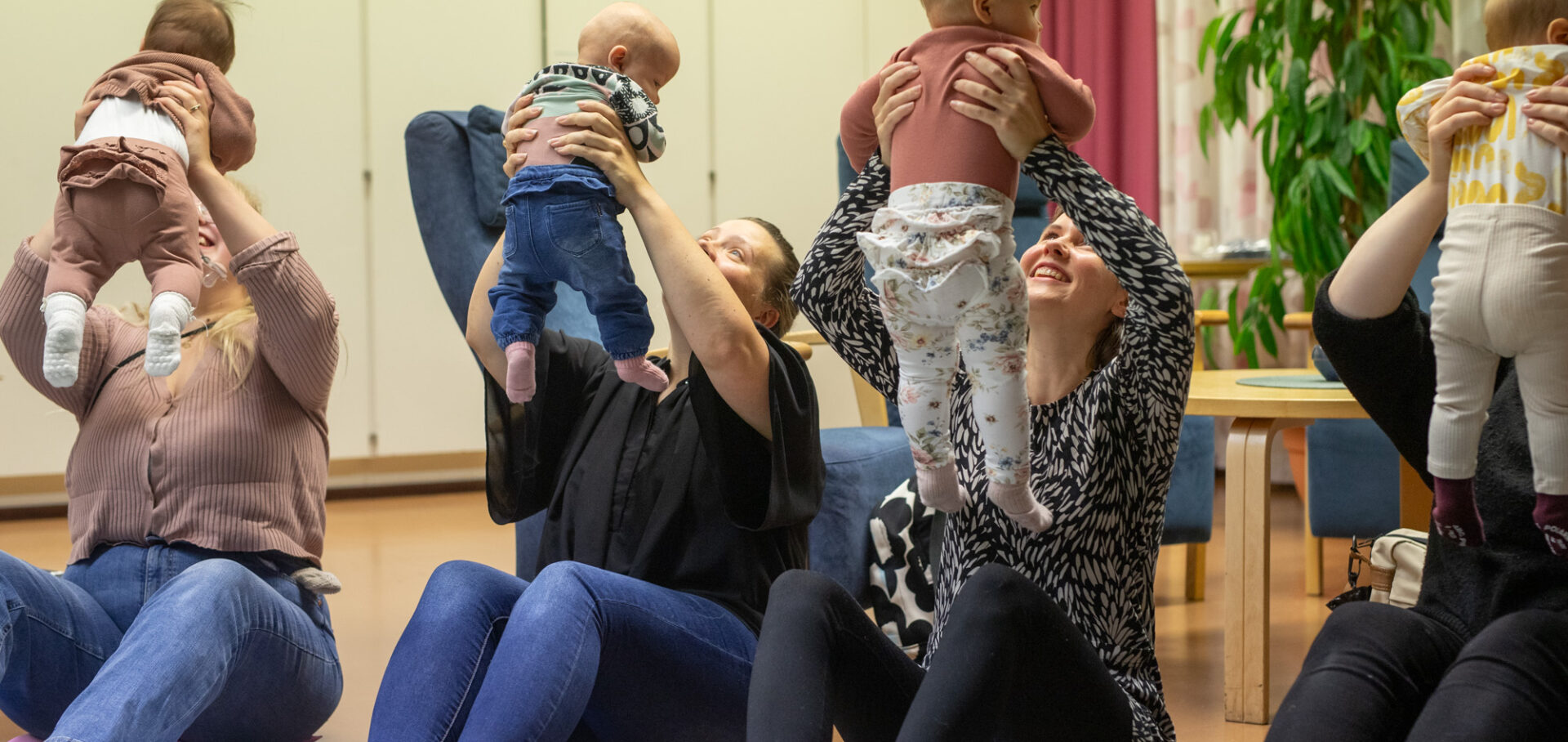äidit istuvat lattialla ja nostavat vauvoja kasvojensa yläpuolelle