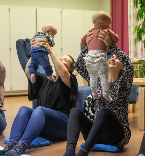 äidit istuvat lattialla ja nostavat vauvoja kasvojensa yläpuolelle