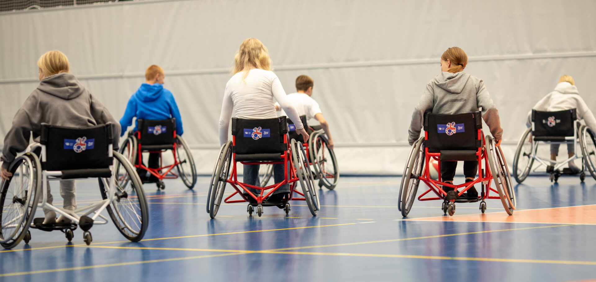 lapsia pyörätuolissa liikuntasalissa takaapäin kuvattuna