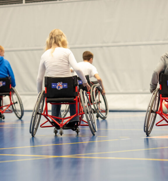 lapsia pyörätuolissa liikuntasalissa takaapäin kuvattuna