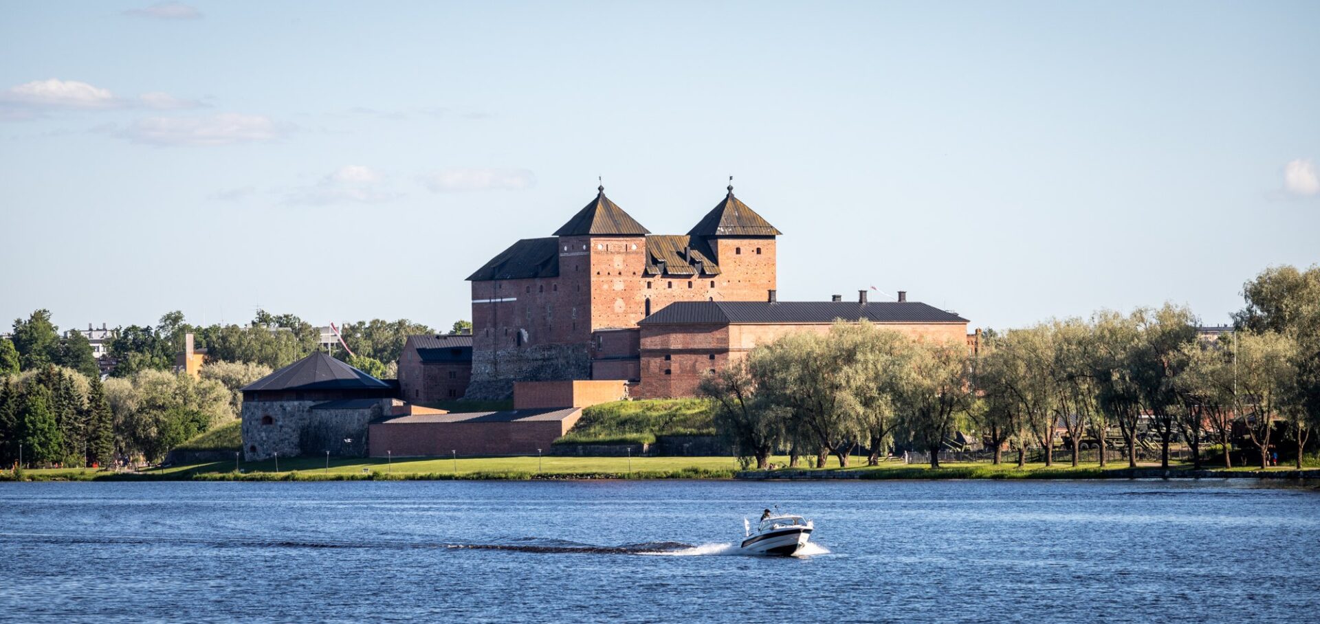 taustalla Hämeen linna ja edessä järvi, jossa moottorivene