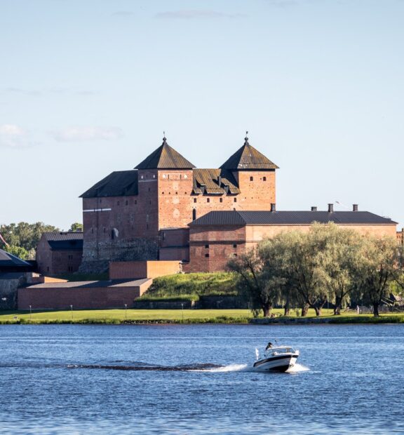 taustalla Hämeen linna ja edessä järvi, jossa moottorivene